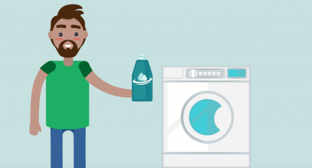 A man holds a bottle of laundry detergent next to a washing machine.